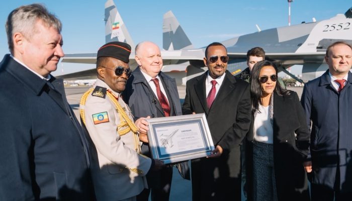 Prime Minister Abiy Ahmed holds a handover certificate in front of an Su-35 fighter jet bearing the Ethiopian flag.