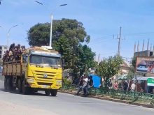 A truck carrying men in military-style uniforms passes bystanders on a town street