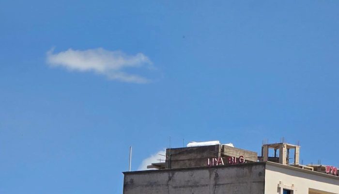An Ethiopian Airlines propeller plane flies low in a blue sky over a building and a hillside billboard.