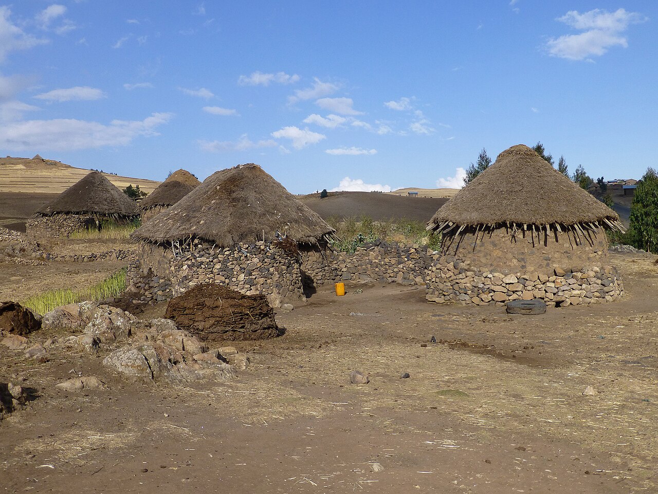 Round stone homesteads with conical thatched roofs on a dry, open highland plain under a blue sky.