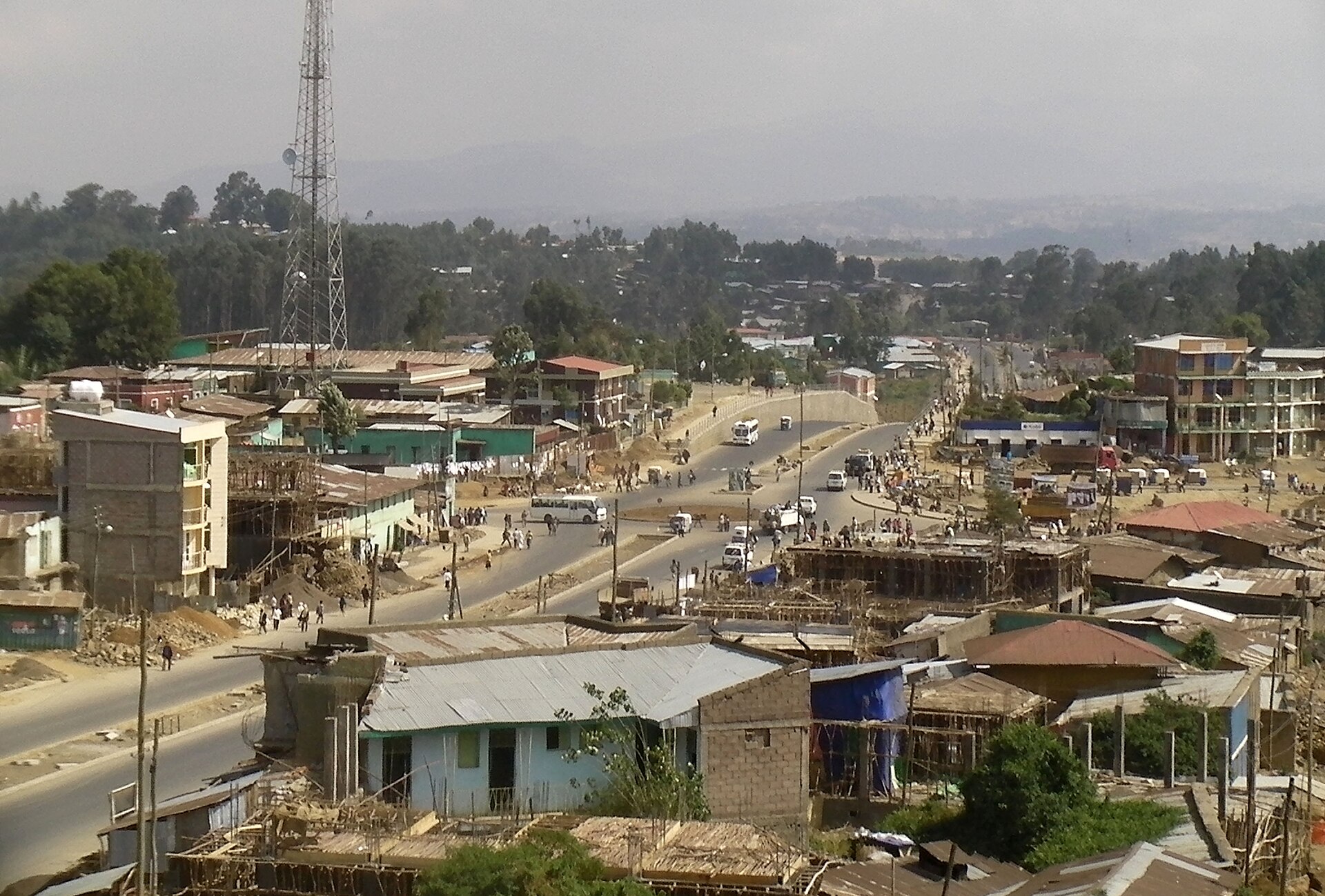 A view over Debre Tabor town, with a paved road, tin-roofed buildings and a telecom tower, and wooded hills beyond.