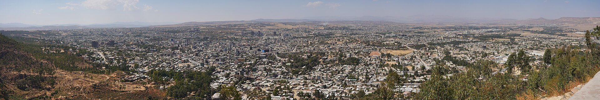 A panoramic view over Mekelle, the capital of Tigray, a wide spread of low buildings and trees beneath hills, seen from a hillside in 2018.